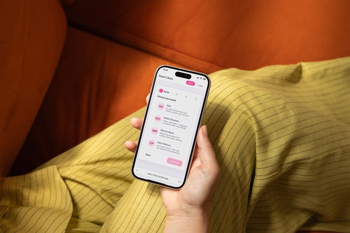 A phone in someone's hand showing a salon's booking page, choosing a stylist.